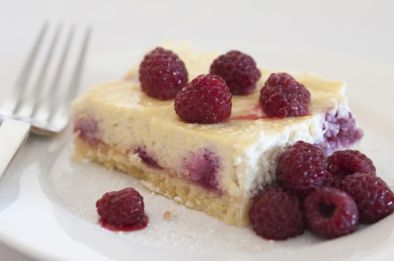 Slice of freshly baked raspberry ricotta cheesecake with fresh whole ripe raspberries served on a side plate