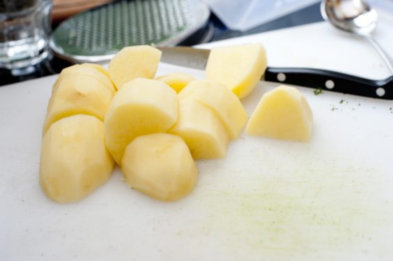 Preparing potatoes for the pot in the kitchen with a pile of peeled, diced potato on the counter top with a knife