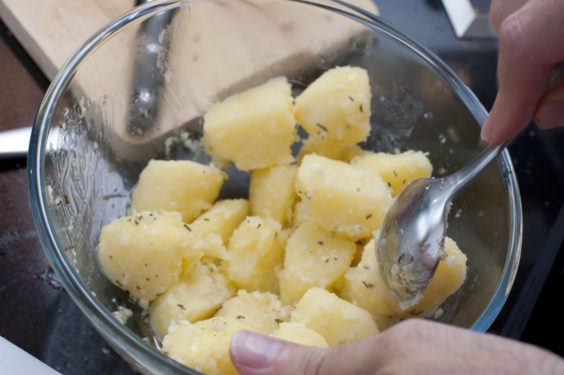 Diced boiled potatoes served in a glass bowl with a hand holding a spoon ready to serve them as a vegetable accompaniment to a meal