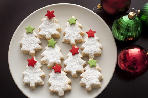 Decorated Christmas tree cookies each with a colourful star at the top arranged on a plate, overhead view on a dark background